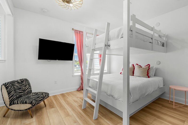 Cozy and stylish upstairs queen-over-queen bunk room with zebra chair, smart TV, and pink accents—perfect for groups vacationing near Destin or 30A.