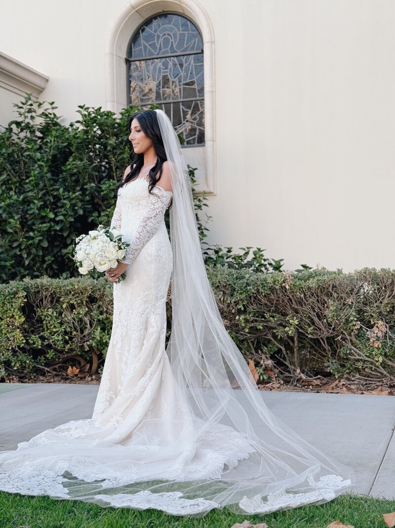 Bride in her wedding gown holding bouquet outside The Immaculata Catholic Church on the University of San Diego's campus.