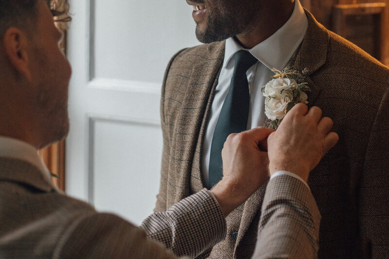 Wedding photography captures best man placing a flower onto the grooms dinner jacket in a stately home setting.