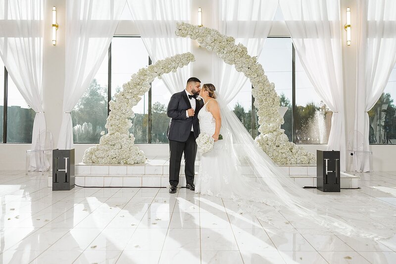 Bride and groom under white floral wedding arch