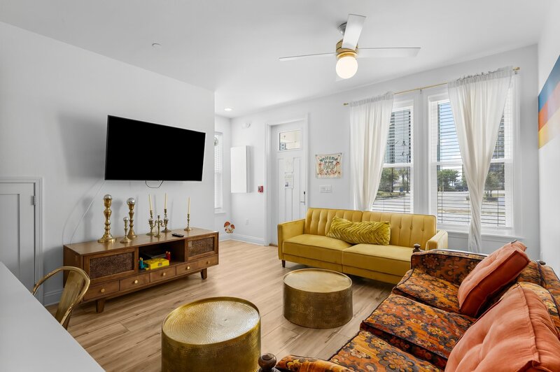 Stylish living space with vintage furniture, large windows, smart TV, and bold 70s rainbow wall art in a family-friendly vacation rental.