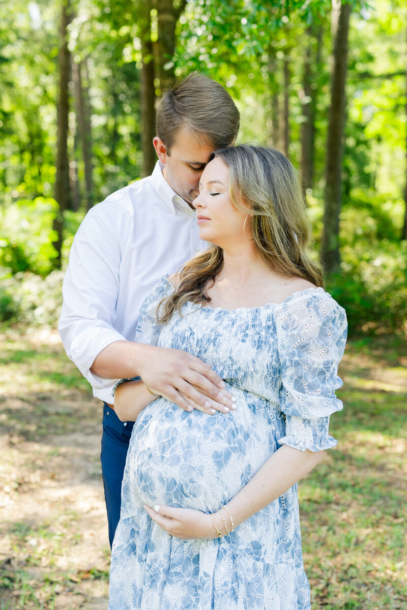 Man snuggling woman while holding pregnant belly during maternity photography session
