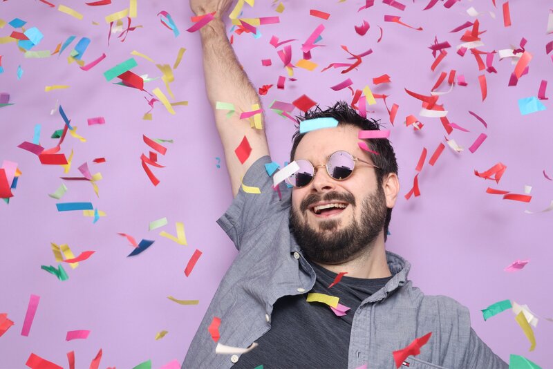 Man smiling and celebrating while confetti falls in front of a purple backdrop at corporate event in Phoenix Arizona