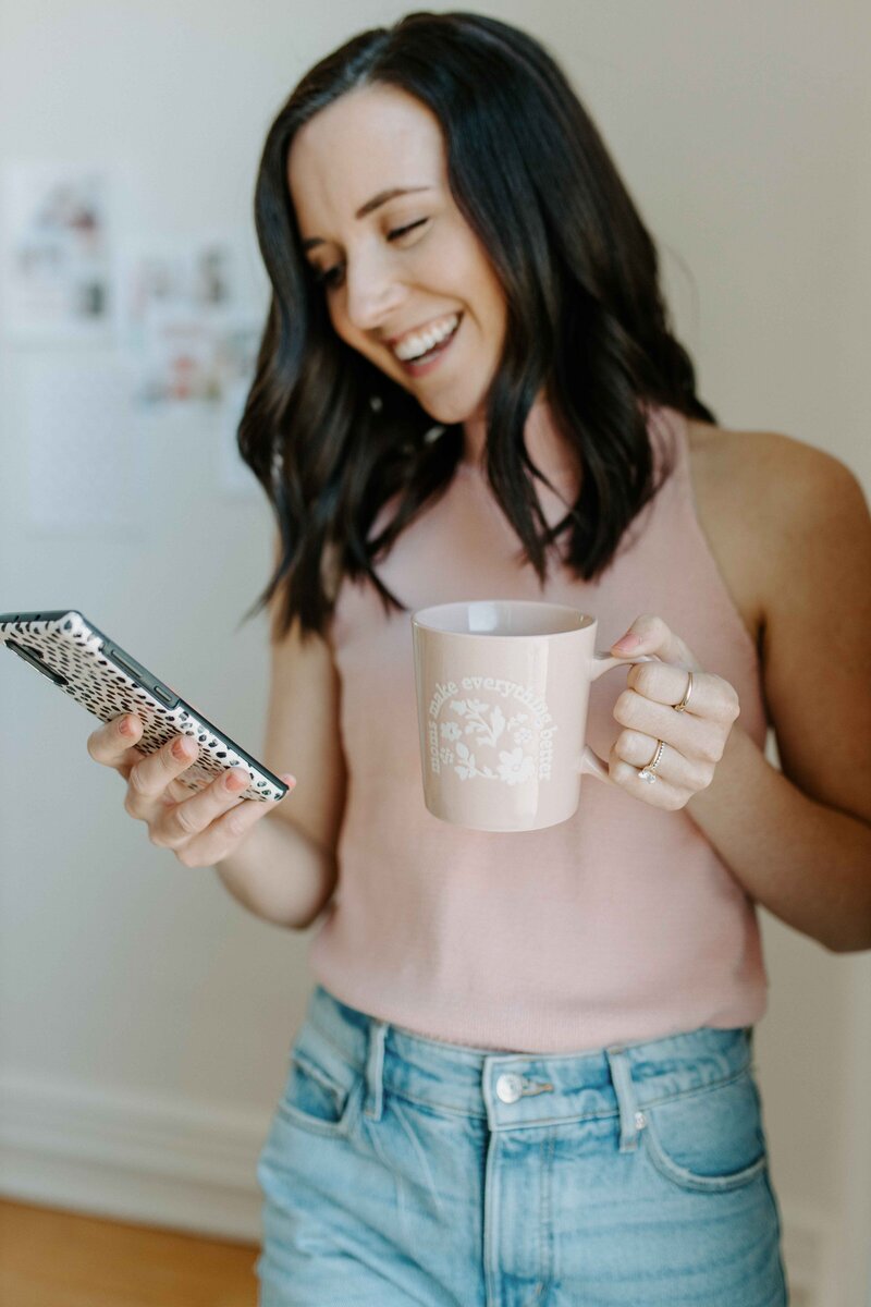 Woman with dark hair smiling at her phone with polkadot case and holding pink coffee mug