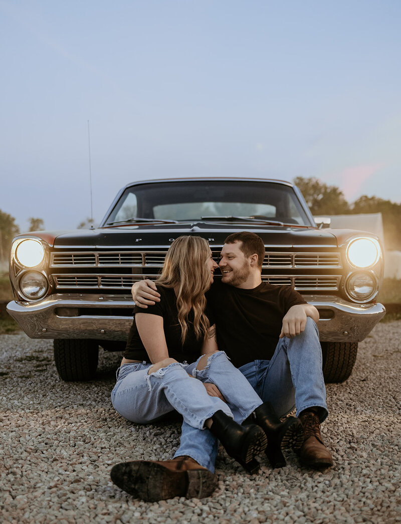 fun blue hour engagement photos with man and woman cuddled together in front of old car