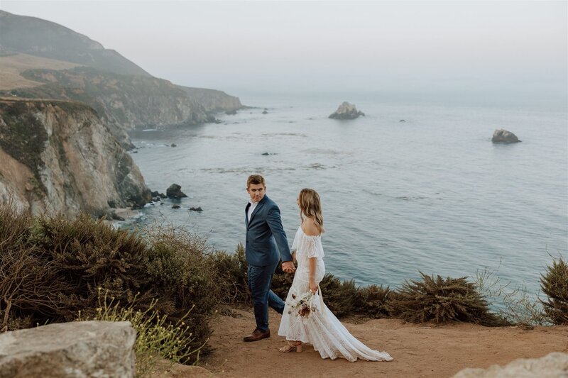 bride and groom walking on a cliff overlooking the ocean