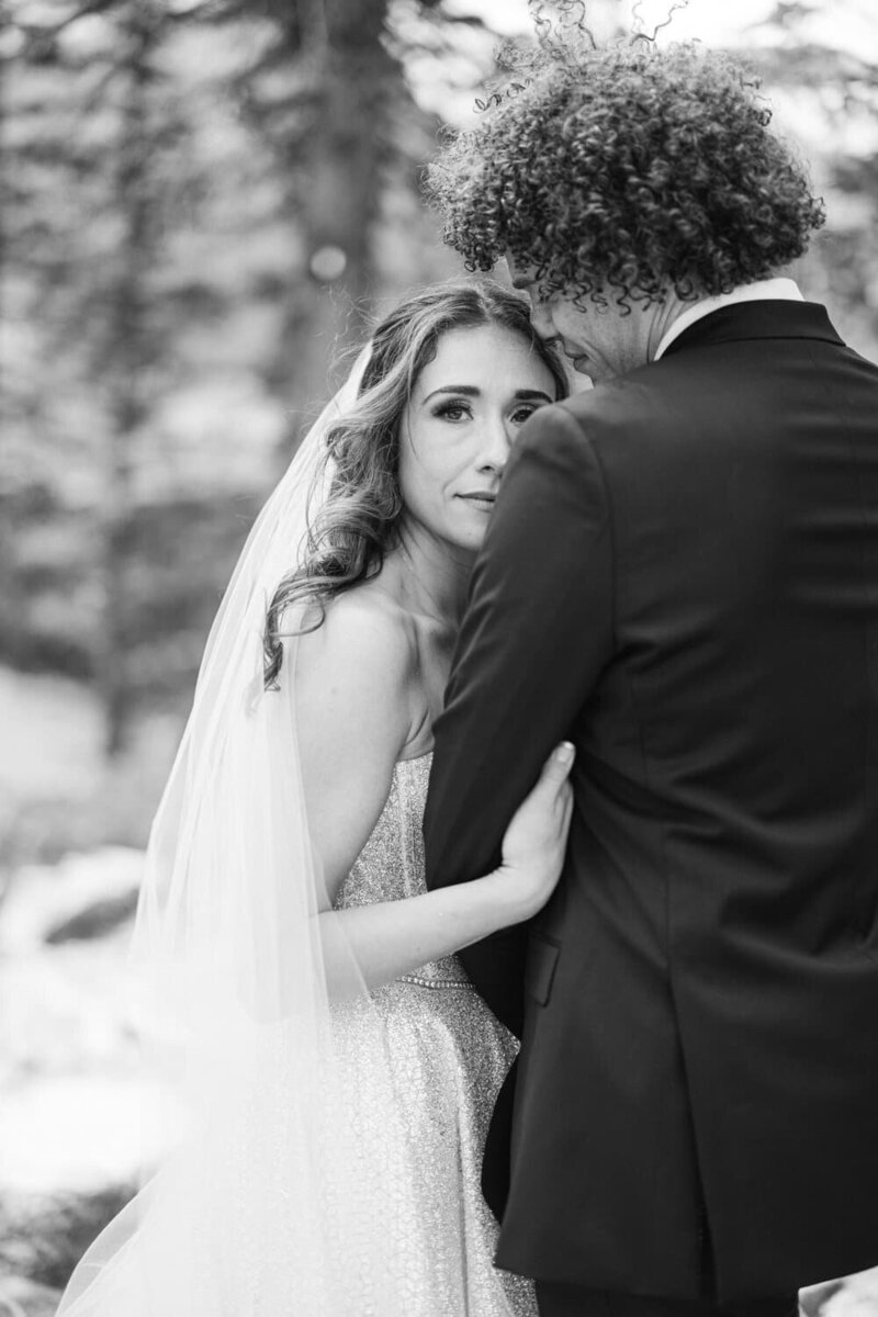 This captivating portrait features a bride holding her groom's arm at Moraine Lake, Banff National Park. With the stunning turquoise lake as a backdrop, the bride gazes into the camera, creating an intimate and timeless moment amidst the breathtaking scenery.