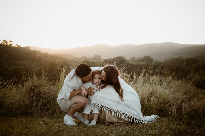 Family wrapped up in blanket at Ormeau Fields at Brisbane near the Gold Coast, having a big cuddle with a beautiful view behind them