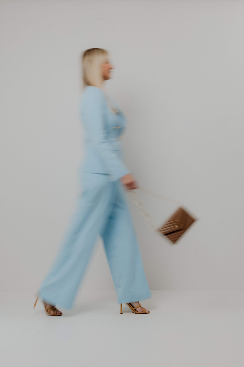 A women walking in a blue suite swinging a brown purse.