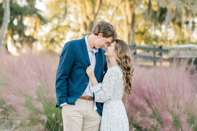 Engaged couple in front of pink grass plants holding each other for engagement photos