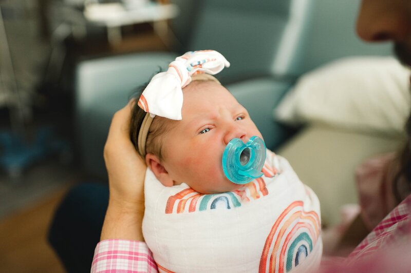 newborn baby in rainbow swaddle with pacifier in mouth at her Houston Newborn Photography session
