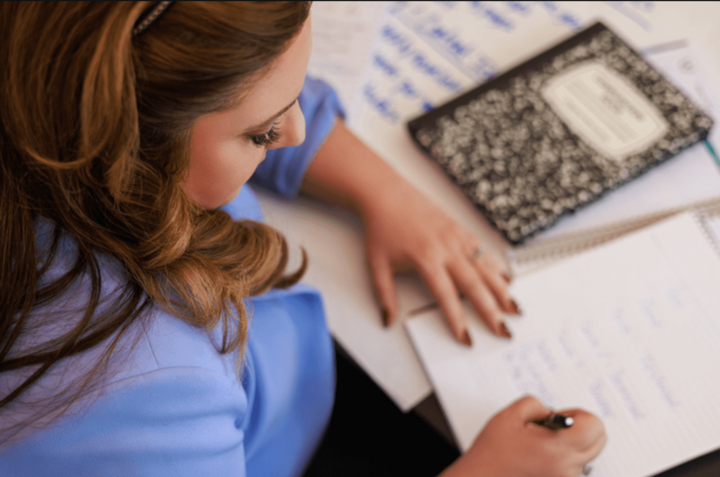 woman at desk writing with paper ipad on desk