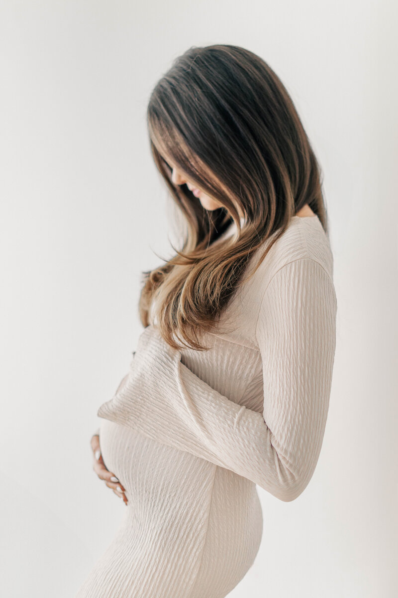 Side profile of an expecting mother in a fitted cream dress gently holding her baby bump, captured during a Kansas City maternity photography session.