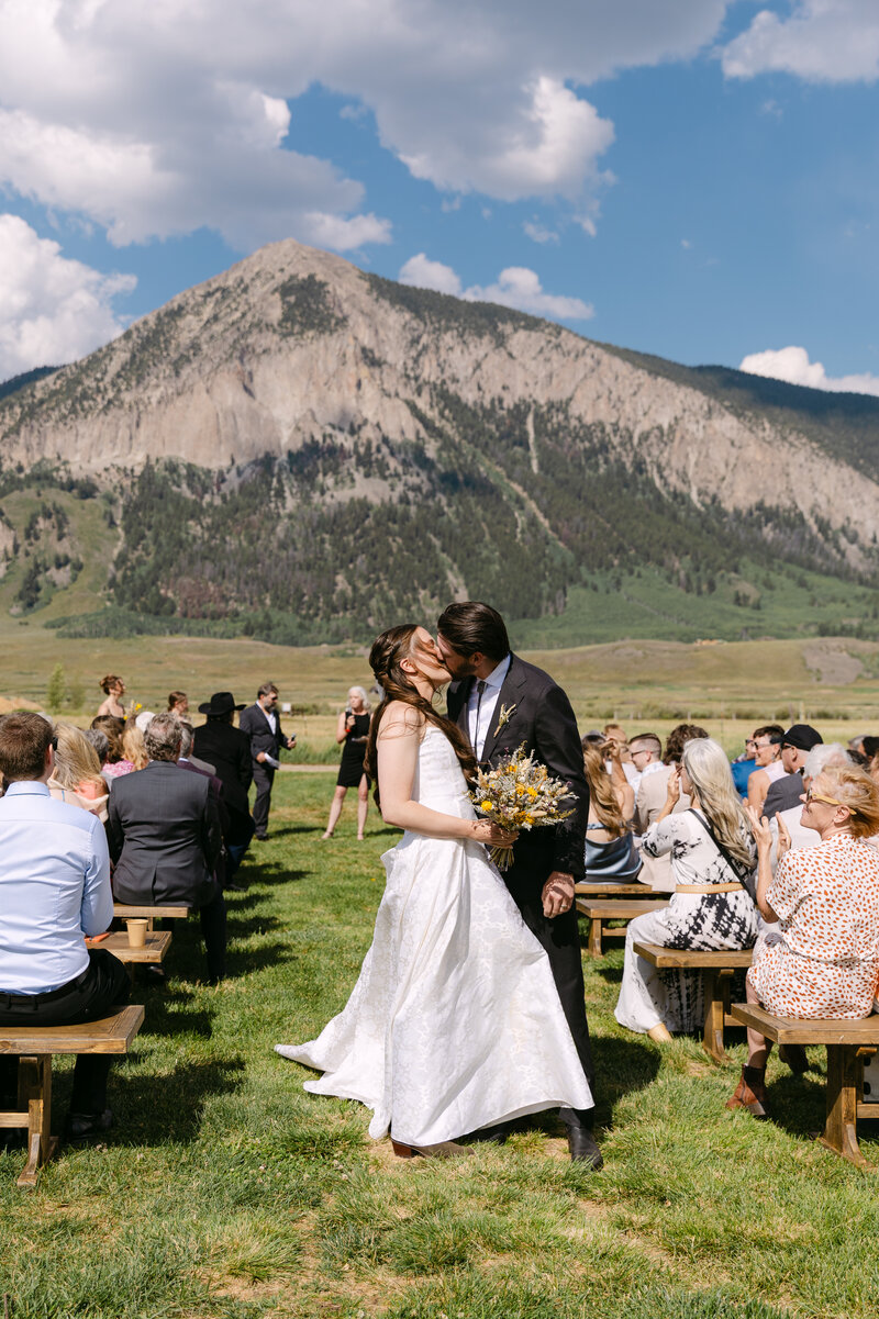Outdoor Colorado mountain wedding ceremony with couple standing under a wooden arch in front of distant peaks – Colorado wedding venue in Crested Butte