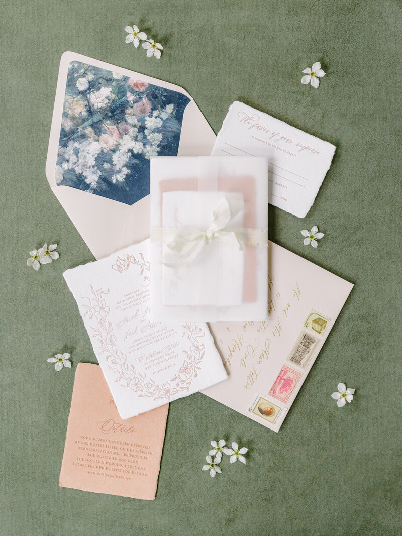 Flat lay photograph for a destination wedding in New England with cream toned invitation suite on an olive green background.