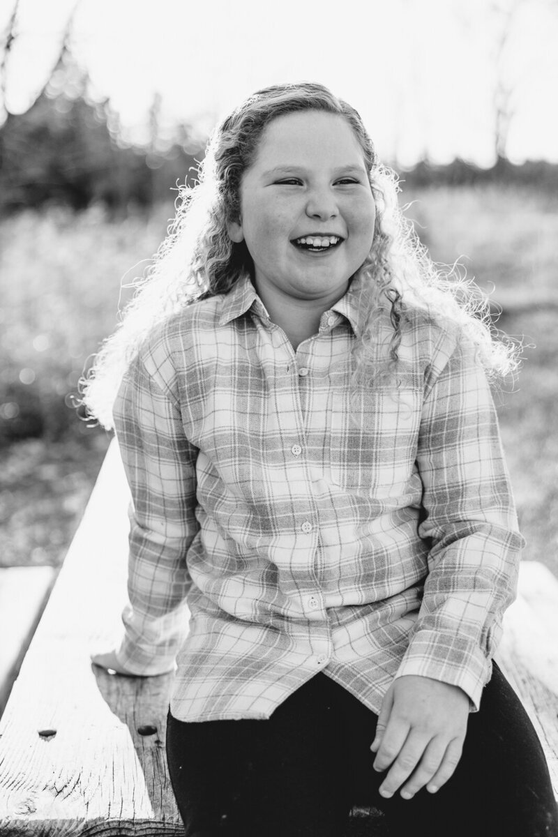 Black and white portrait of child sitting on a picnic table laughing. 