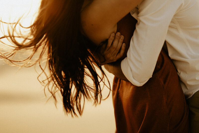 A close up photo of a couple embracing each other on a windswept day at Silver Lake Sand Dunes.
