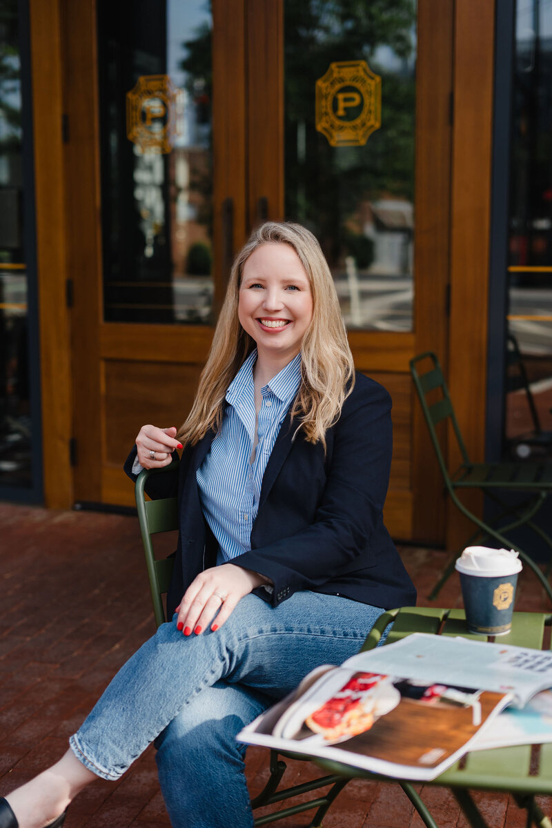 Headshot of Anna Bradshaw sitting at an outdoor cafe table with magazines and a coffee