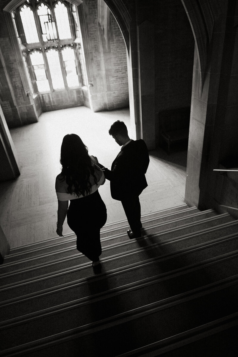 artistic black and white image of couple walking down historic staircase at the university of toronto's hart house