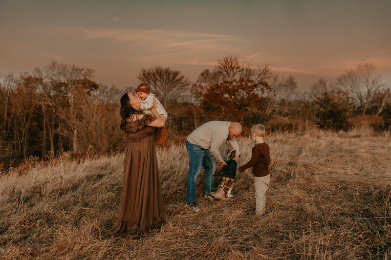Family enjoying a playful outdoor sunset session in Peapack, NJ, with parents and children interacting joyfully in a grassy field, captured by Burkat Photography.