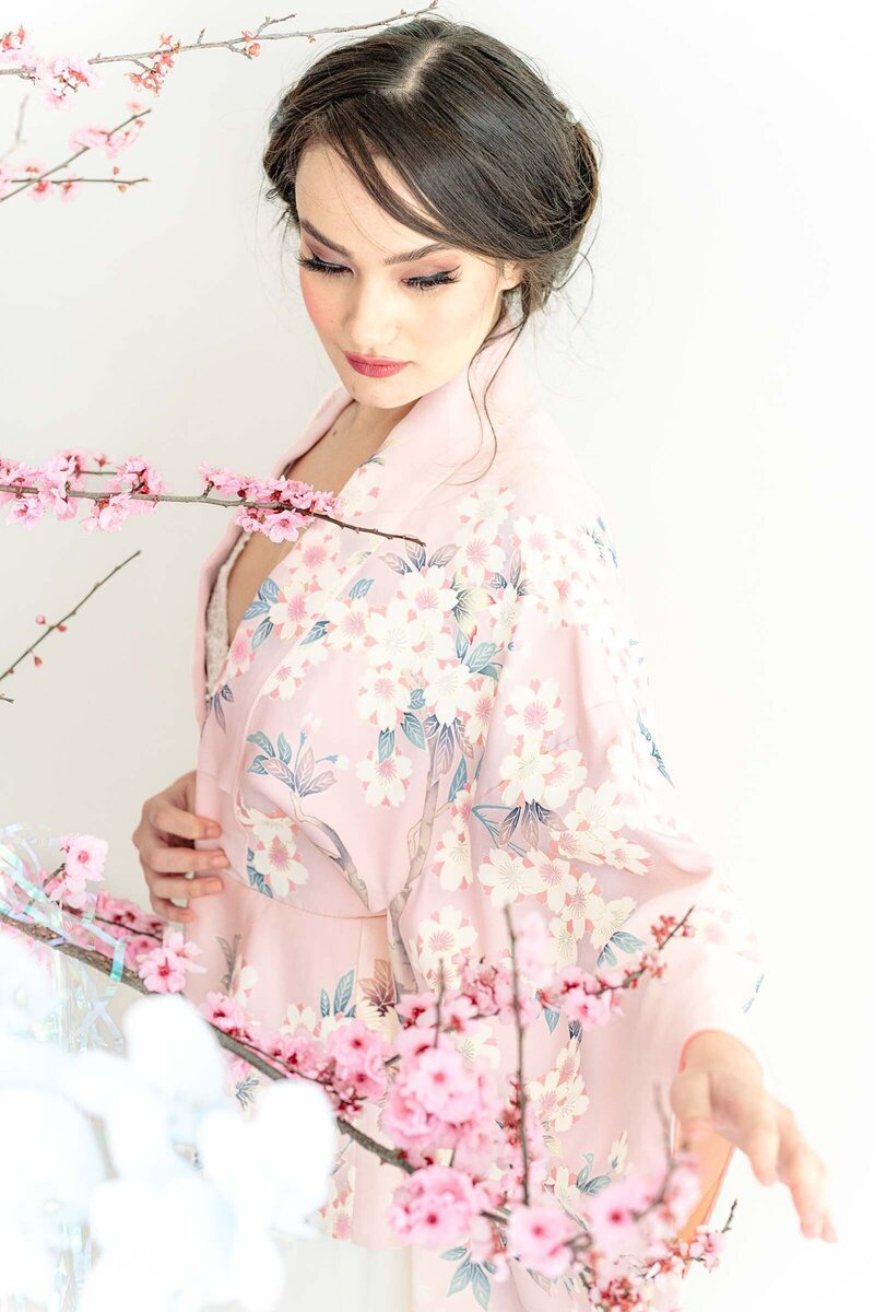 Bride in soft pink cherry blossom kimono surrounded by blooming branches during Japanese-inspired spring wedding shoot
