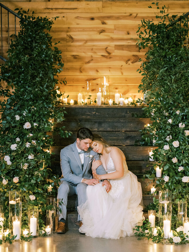 Newlywed bride and groom sit together on romantic candlelit stairs