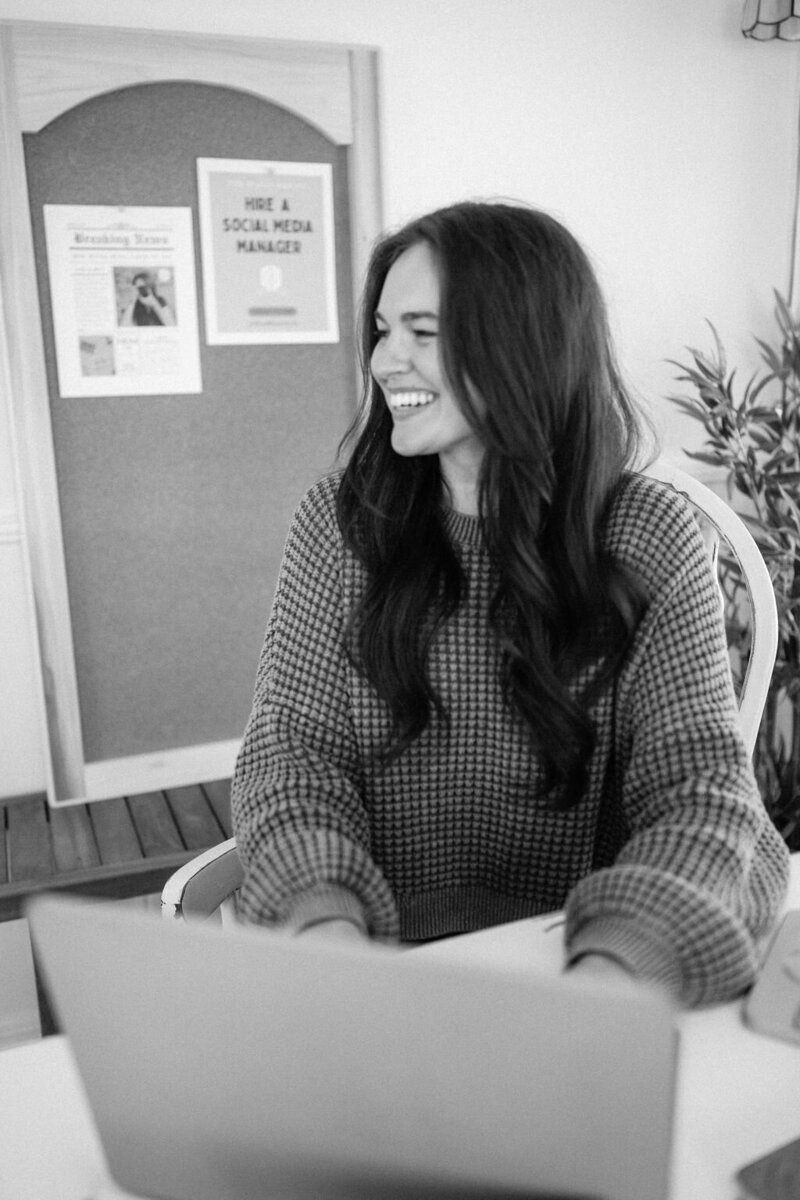 a black and white photograph of a woman gazing left while working on her laptop