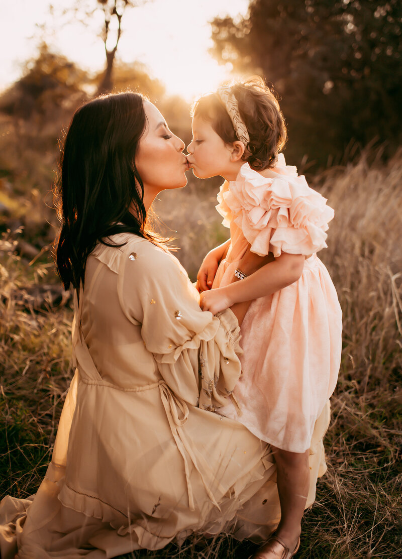 Mother kissing her daughter in golden fall light