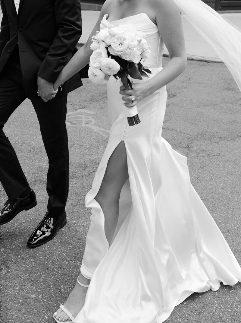 The groom and the bride are walking down the street while holding hands