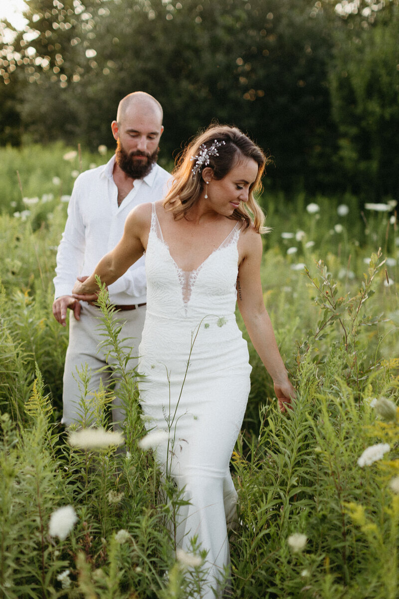 A bride and groom wander through a field of flowers—a perfect moment captured by PEC destination wedding photographer, Jennifer van Son at 100 Acre Wood in Picton