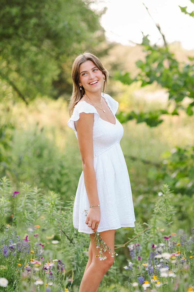 Senior girl in a white dress standing in wildflower, smiling by Hershey PA photographer