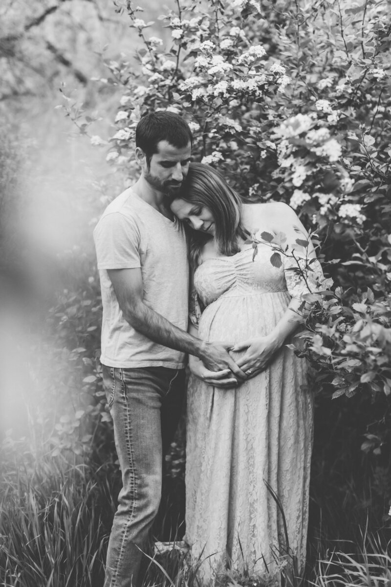 black and white photo of a maternity shoot while wife and husband stare at bump