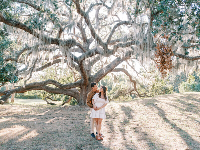 Couple standing beneath a sprawling oak tree draped in moss at Philippe Park