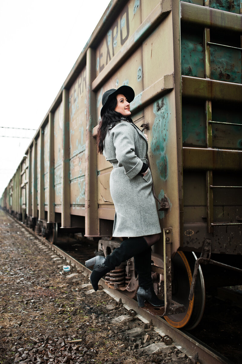 Author standing on a train wearing boots, an oversized hat, and grey winter jacket