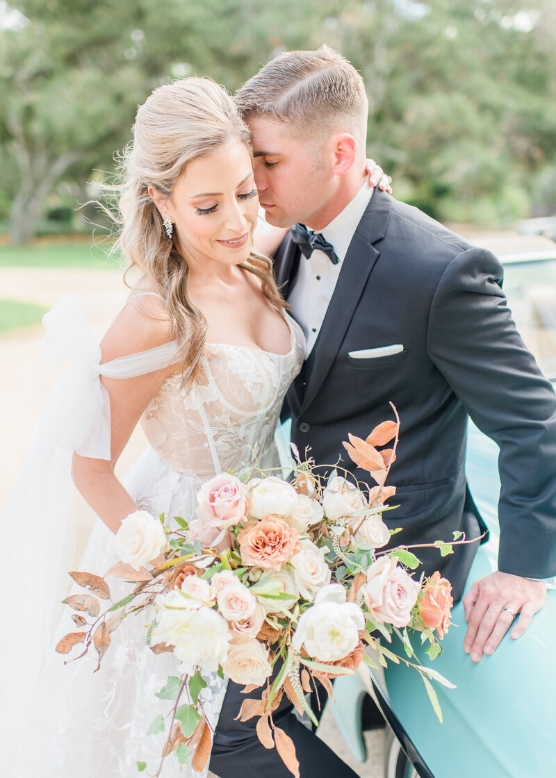 Wedding Photographer, Groom leans into bride sweetly, she smiles in her wedding dress and with bouquet