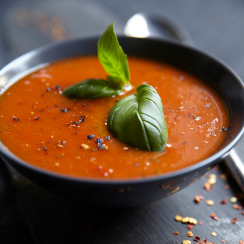 A bowl of rich tomato soup garnished with fresh basil leaves