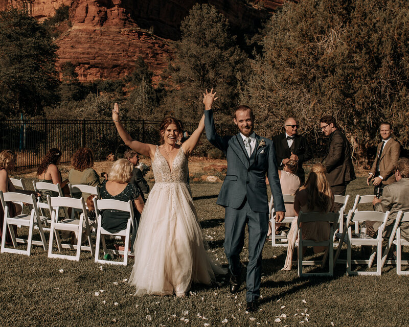 bride in sparkly sleeveless and tulle gown and groom walking down the aisle with red rocks in the background at enchantment resort