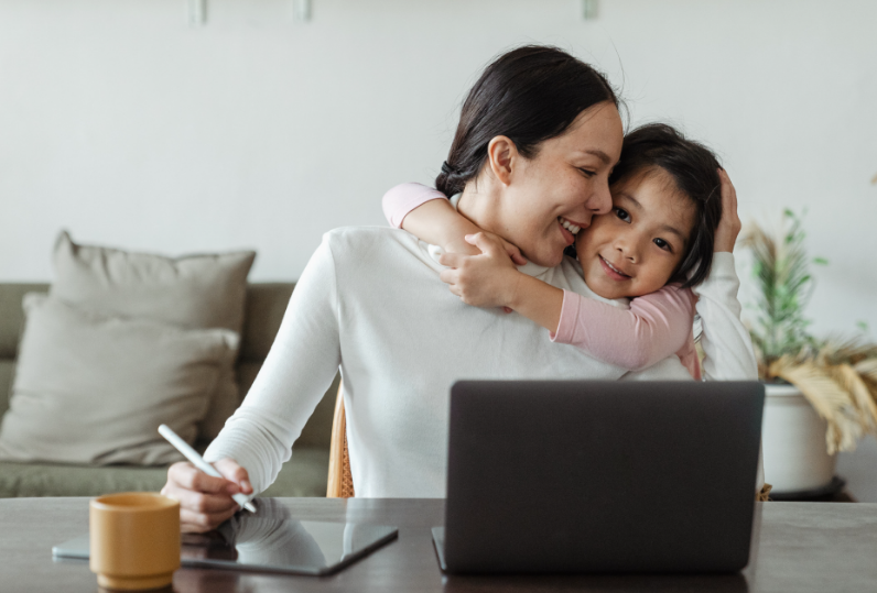 A young girl hugs a woman at a desk