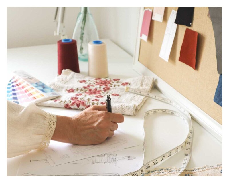 Freelance fashion designer Doreen sketching women's apparel designs at her studio desk with fabric swatches and color samples for a new collection.