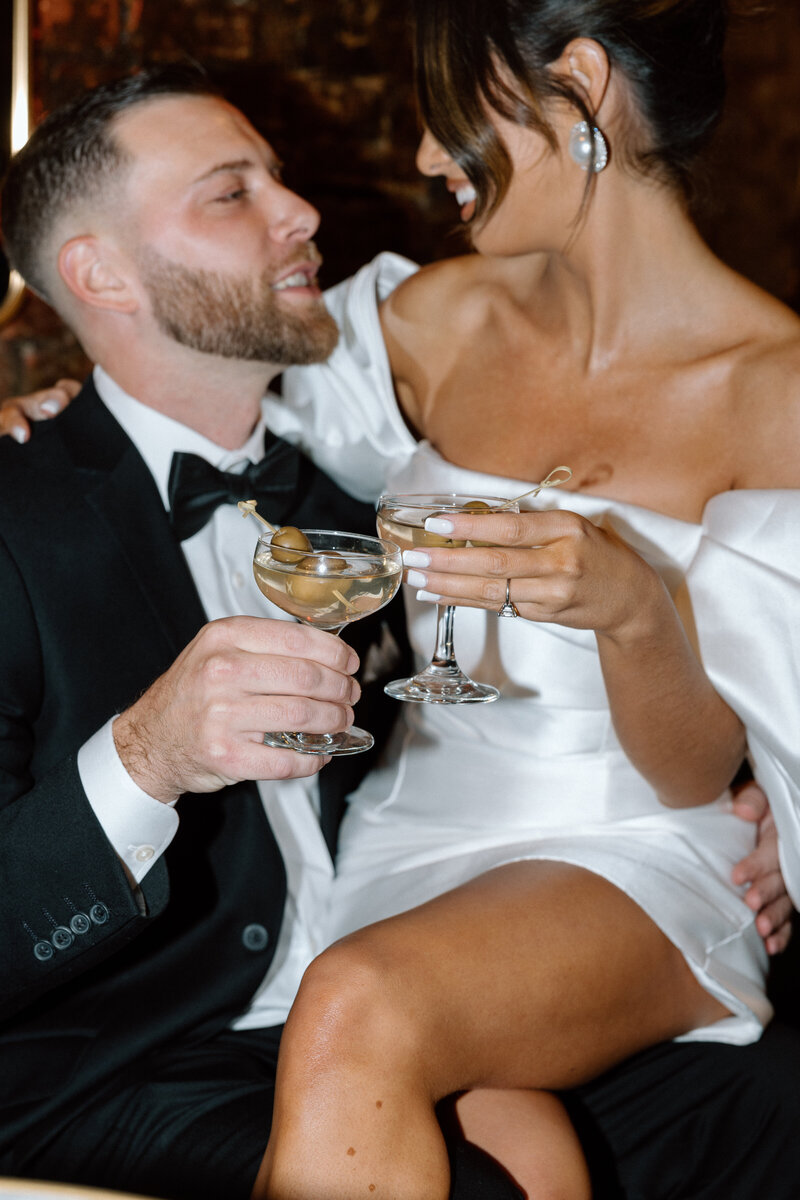 Bride sitting on groom's lap toasting martinis at underground bar in Philly