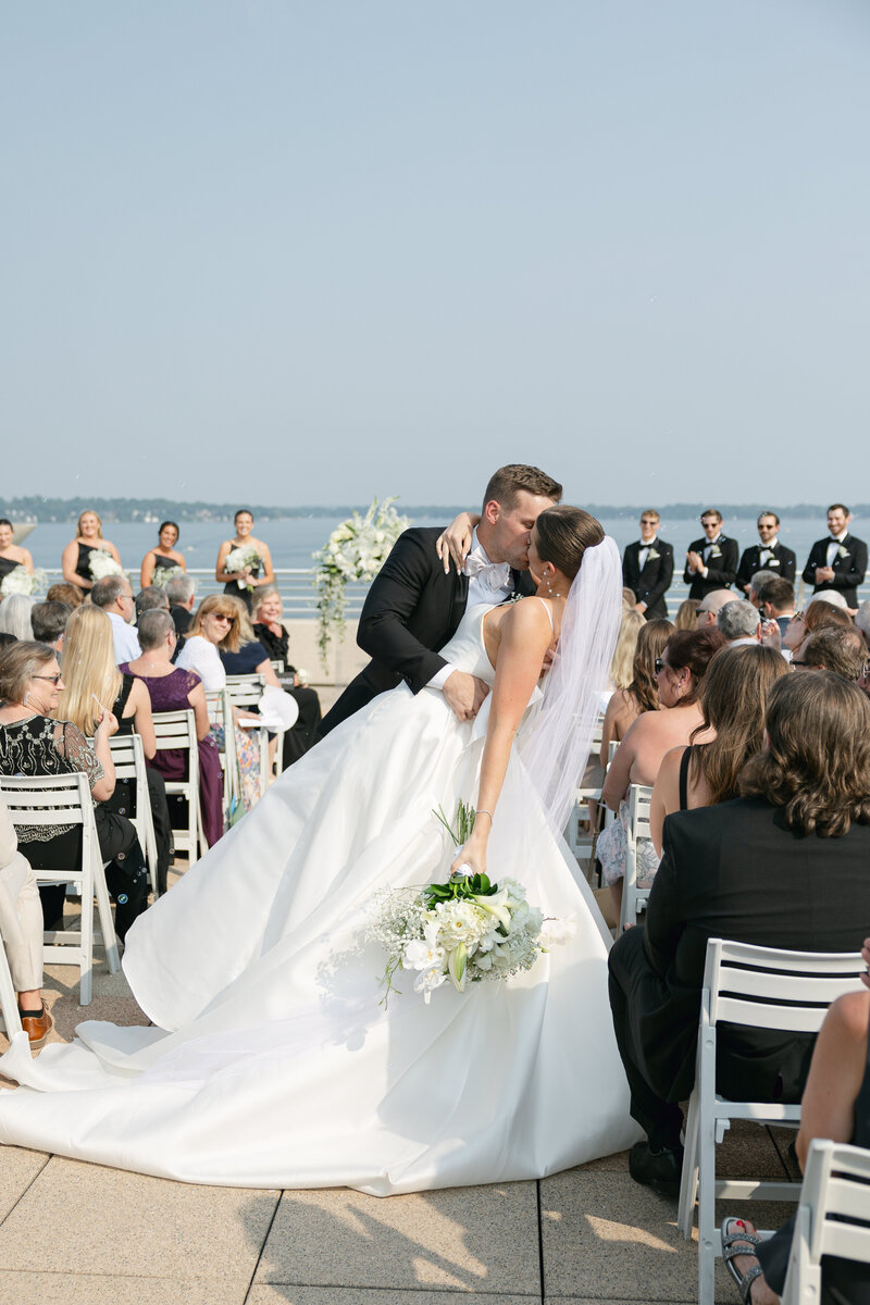 Bride and groom kissing at wedding ceremony with lake background in Wisconsin.