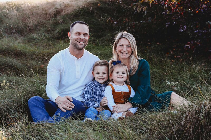 Mom, dad, daughter, and son sitting in grass field during family photo session.