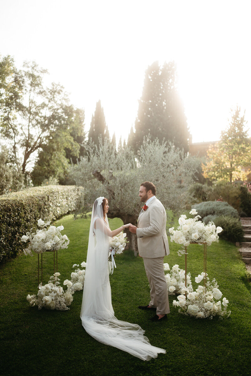 Bride and groom stand in front of an olive tree in a Tuscany villa, framed by floral arrangements for their elopement ceremony | Eloping Ideas 