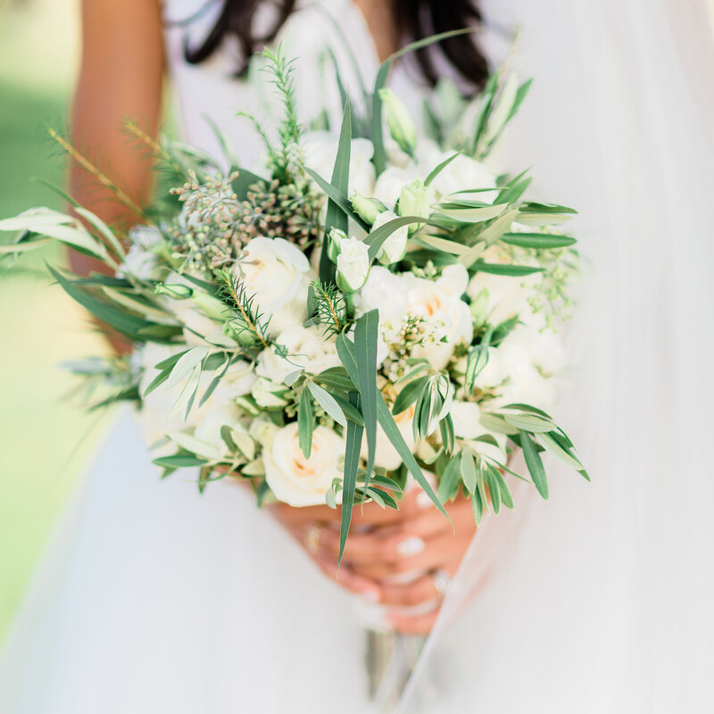 bride holding a bouquet made of white flowers up close with the bride out of focus in the background