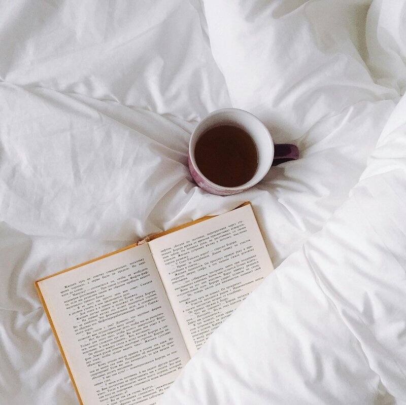 Un livre ouvert sur un lit avec un café posé à côté
