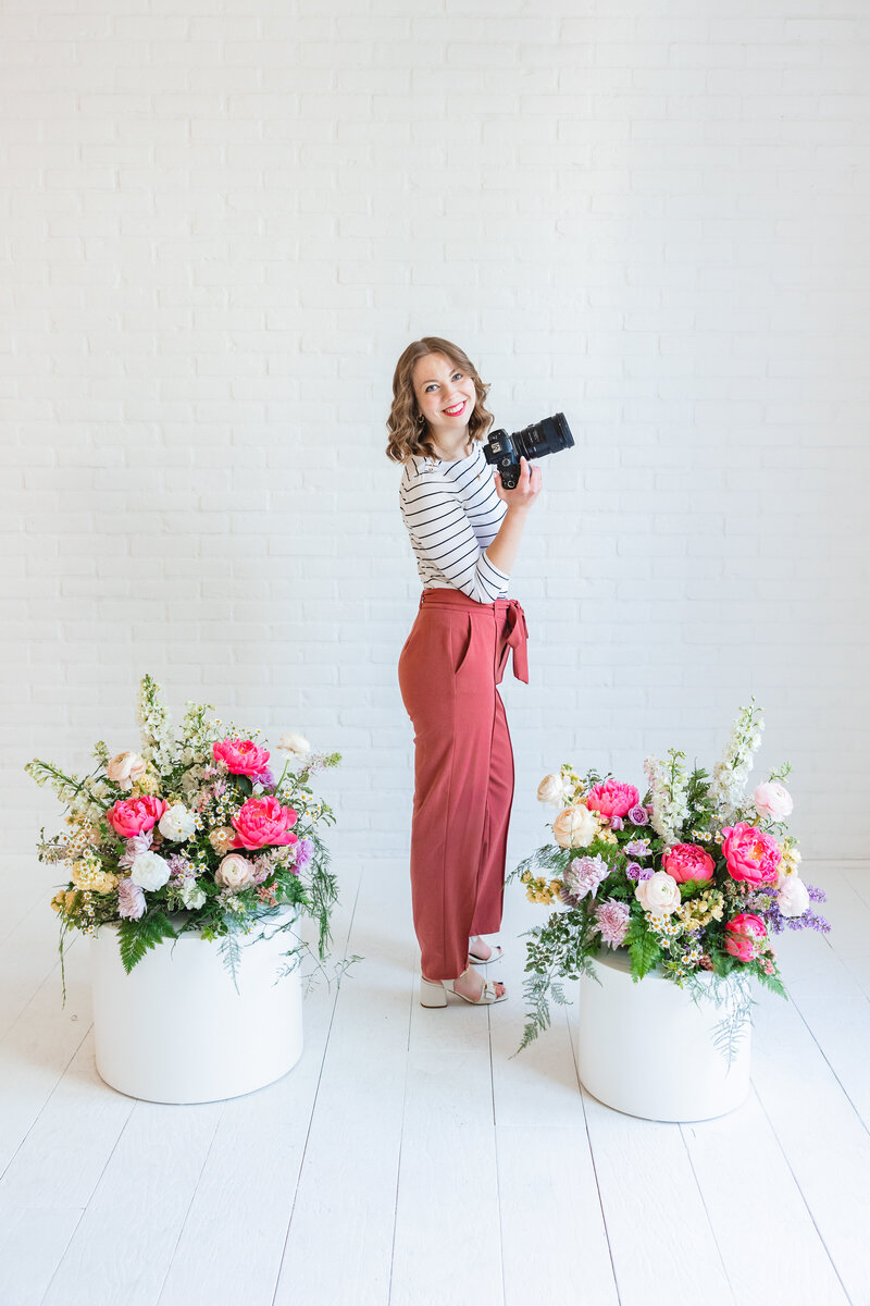 photographer in white jeans with a sunset and pink trees behind her in Boise