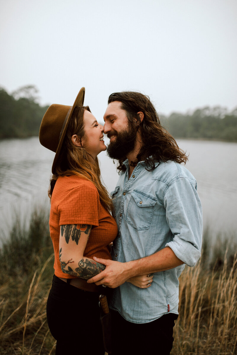 couple embraces, touching noses in natural setting by lake on 30a florida