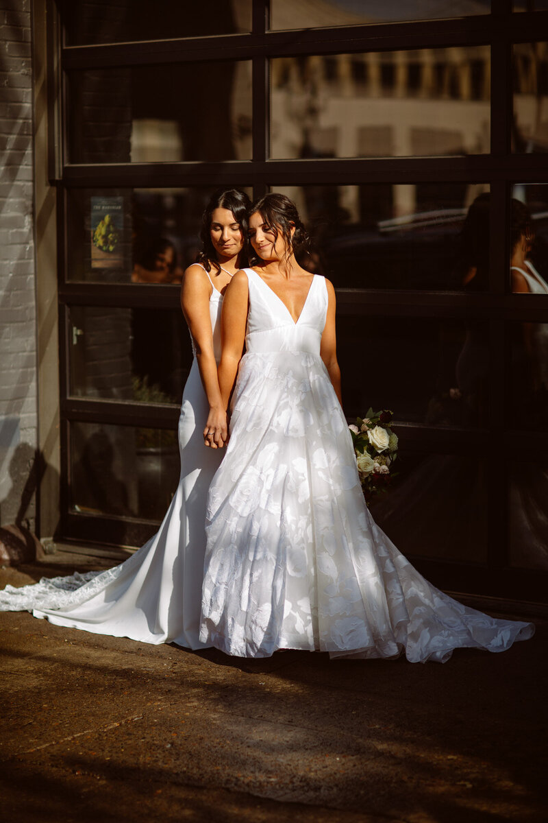 Same sex bride holding each others hand both wearing wedding gowns
