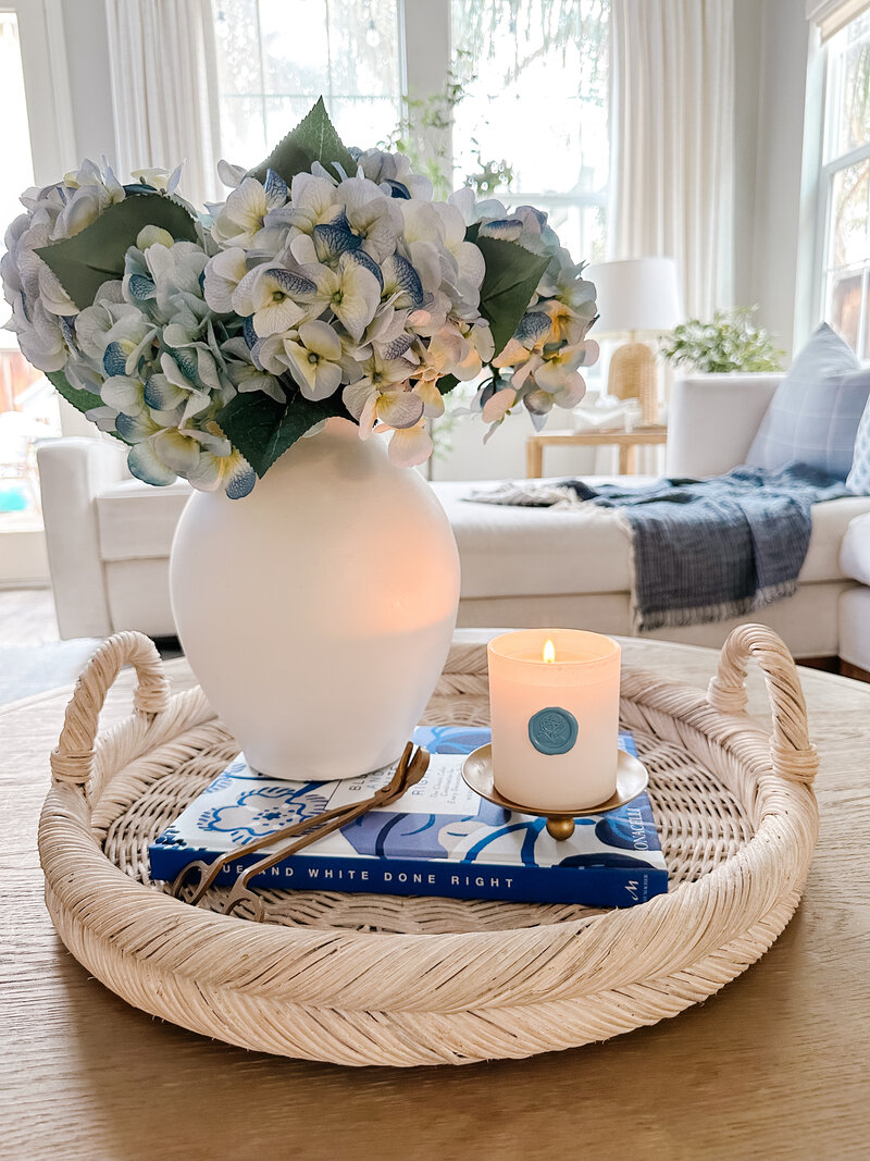 blue hydrangeas in a white vase, a white candle, and a book on a coffee table
