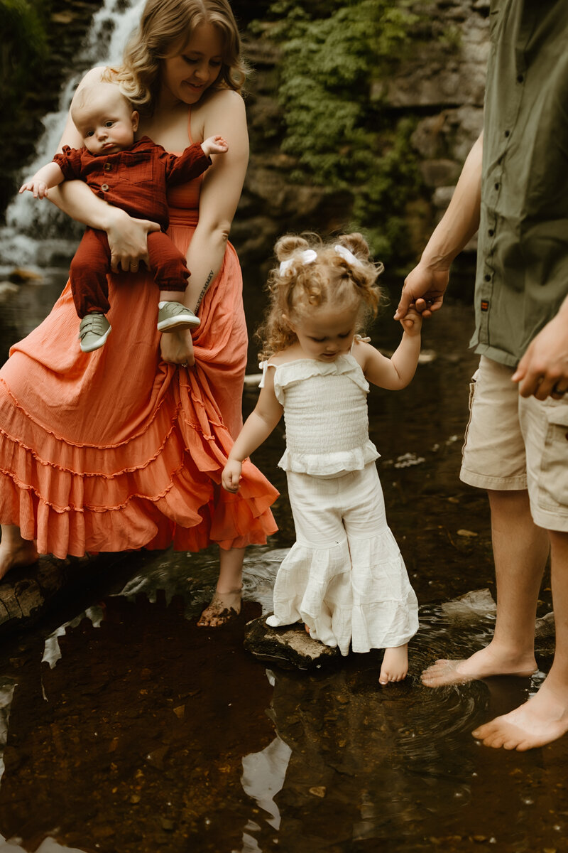 child dipping toes into creek holding on to dad's hand